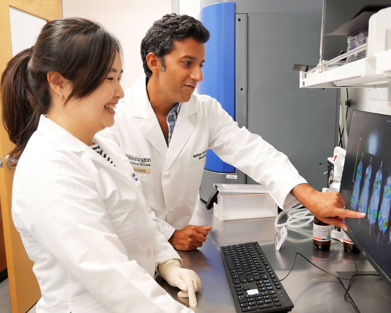 two scientists in lab coats looking at results on a monitor